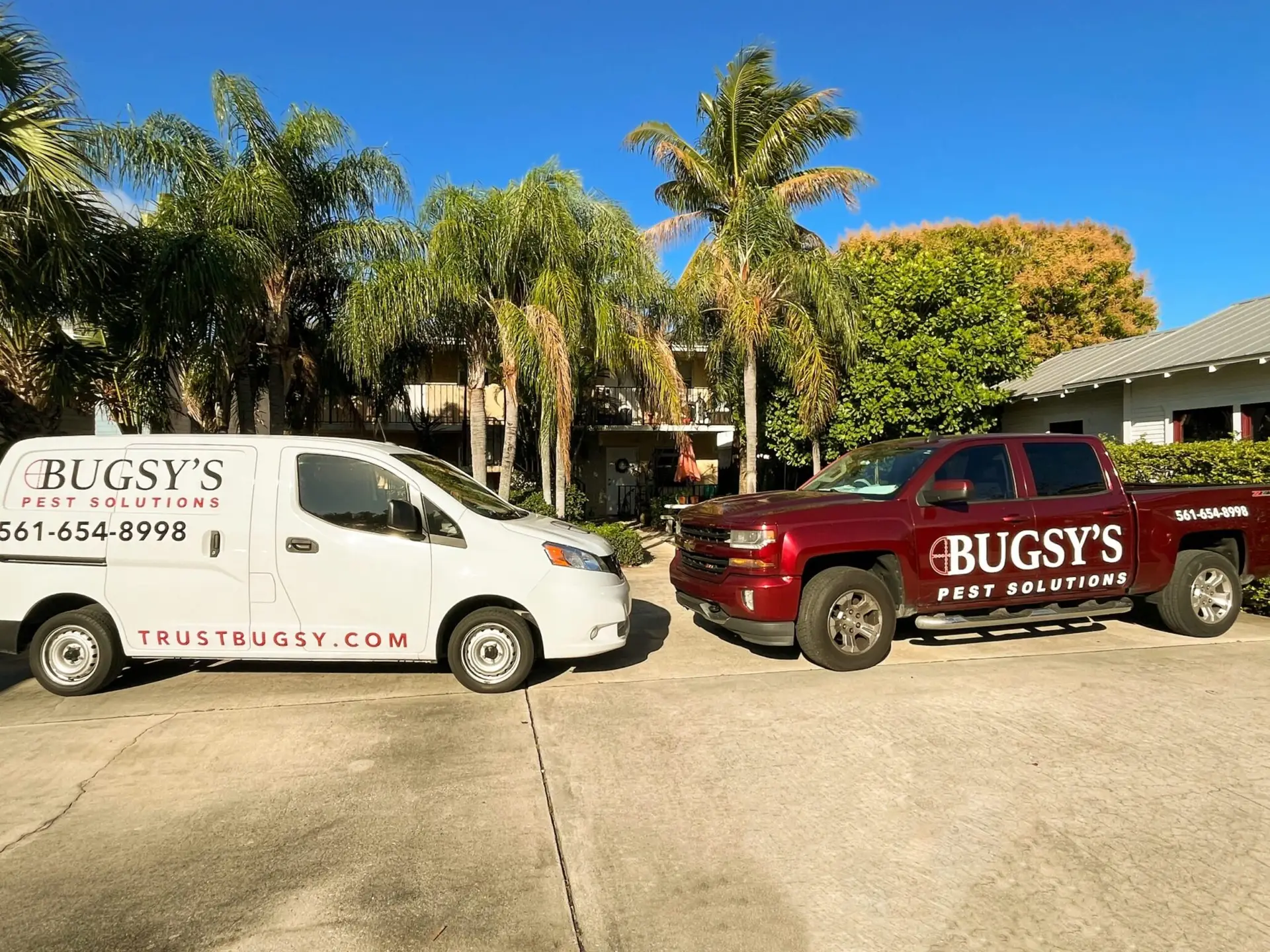 White van and red truck with "Bugsy's Pest Solutions" branding parked in a sunny, tropical setting in West Palm Beach, showcasing pest control services.