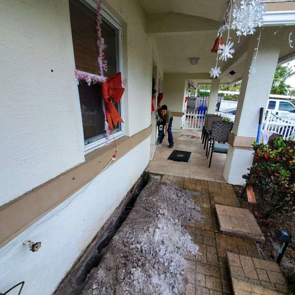 Person inspecting a trench near a home's foundation, revealing soil and construction materials, highlighting pest control preparations in West Palm Beach.