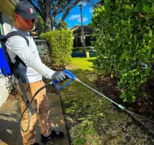 Pest control technician applying treatment in residential yard with backpack sprayer for effective pest management.