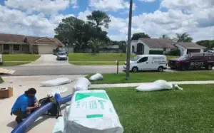 Technician performing pest control service outside a residential property in South Florida, with equipment and materials visible on the lawn.