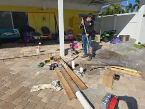 Person using tools in a residential outdoor area, surrounded by construction materials and equipment, related to pest control service preparations.